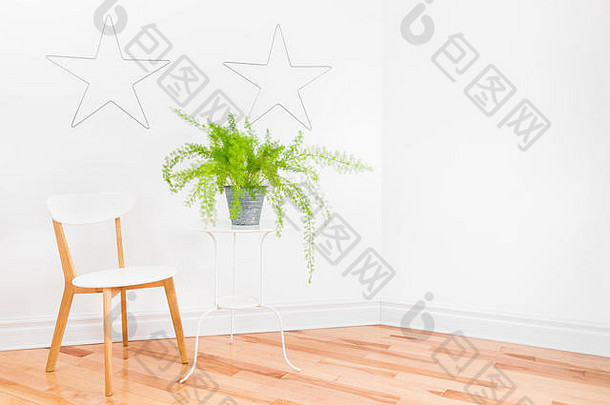 明亮的房间角落用金属星星装饰着白色的墙壁，简单的家具和美丽的芦笋蕨类植物。文本的空间。