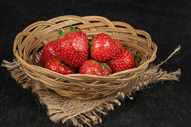 整批新鲜的红色草莓装在圆藤碗里，灰色石头上有黄麻织物