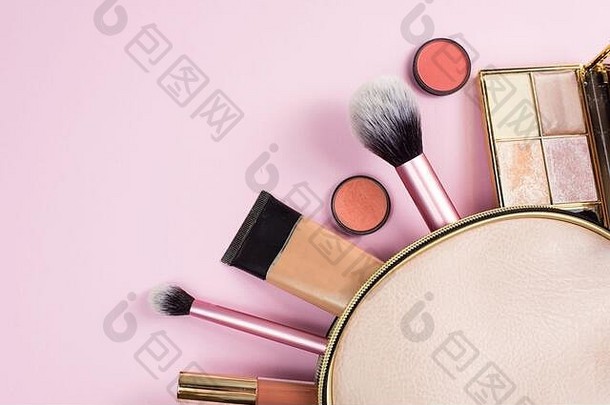 一个米色皮革化妆包的俯视图，化妆美容产品溢出到柔和的粉红色背景上。