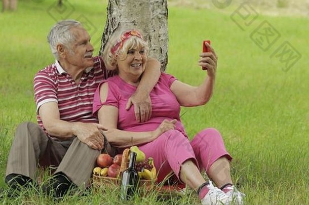 家庭周末野餐。老年人、快乐的高加索人夫妇用智能手机自拍。远程在线视频聊天电话。上了年纪的男人，女人。丈夫和妻子在公园里。祖父母