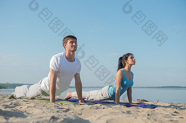 一对年轻夫妇在做伸展瑜伽练习，背景是大海