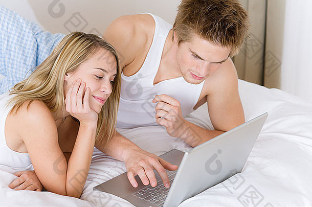 年轻的夫妇放松床上移动PC说谎