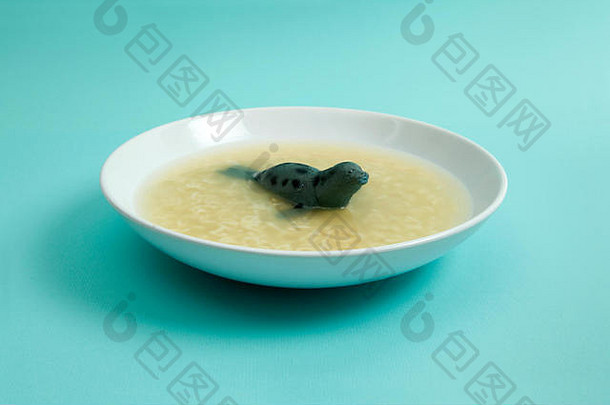 一种海狮动物在带有字母意大利面的肉汤中游泳。古怪、有趣、色彩简约的静物摄影