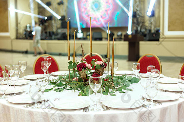 餐厅内装饰华丽的圆形宴会桌。鲜花是金色的蜡烛和红色的椅子。非常富有。