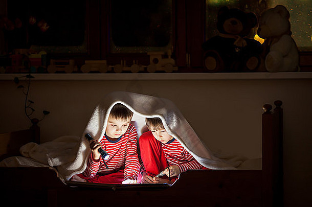 两个可爱的男孩，睡后在床上看书，用手电筒，冬夜