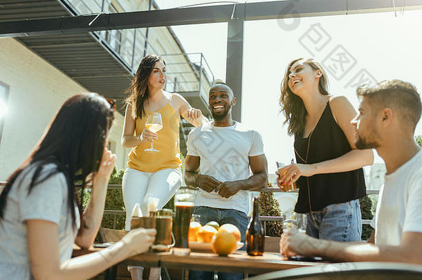 年轻的朋友们一起喝啤酒，玩得开心，欢笑和庆祝。在阳光明媚的日子里，女人和男人都戴着啤酒杯。啤酒节，友谊，团结，幸福，夏日概念。