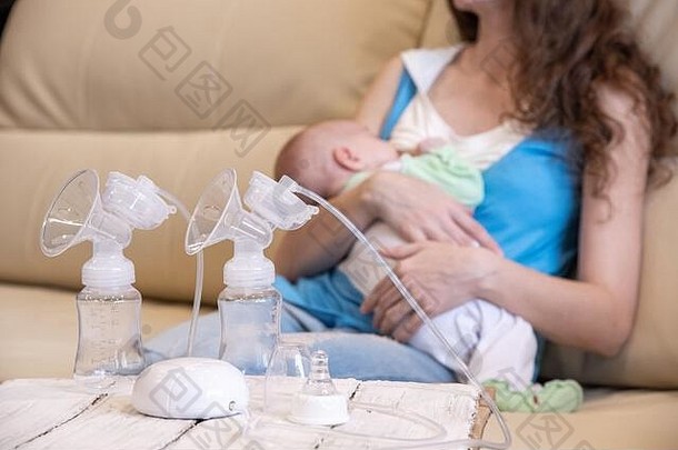 一位年轻的母亲正在哺乳她的婴儿，一台电动吸奶器正站在她面前的一张木桌上