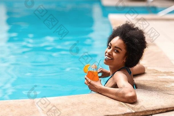 美丽的黑人女士在<strong>游泳</strong>池里喝着美味的鸡尾酒，在炎热的<strong>夏日</strong>里放松，自由活动