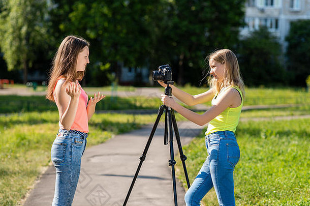 十几岁的女孩夏天公园记录视频相机在情感上gesticulates手相机三脚架