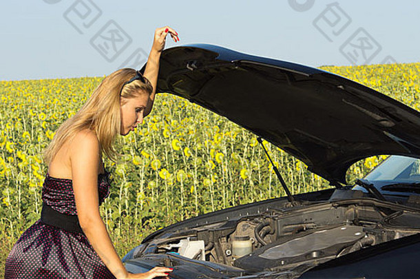 一位穿着漂亮衣服的女士在车上升起的引擎盖下检查，试图确定故障原因，背景是一片向日葵。