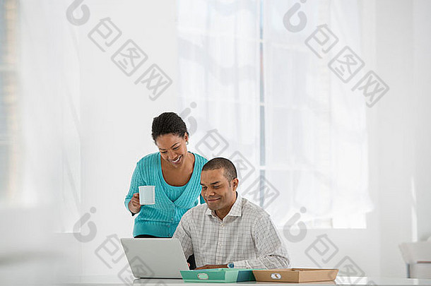 商业一个女人端着一杯咖啡，一个男人看着一台笔记本电脑。