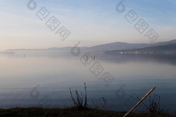 特拉西门诺湖（意大利翁布里亚）的美景，群山和蓝天映在水面上，前景是岸边的一根木杆
