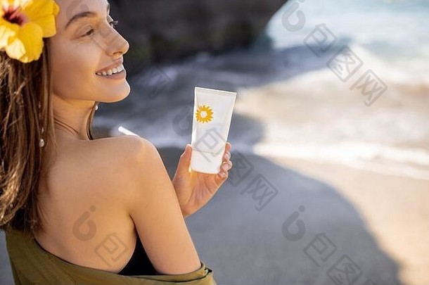 一个美丽的年轻女子，在夏天的海滩上休息时，拿着装有防晒霜的发花托。皮肤防晒理念