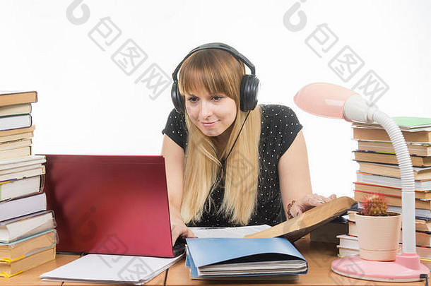 快乐的学生，戴着耳机坐在桌旁，用笔记本电脑寻找你需要的信息