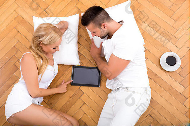 一对漂亮的年轻夫妇坐在<strong>新</strong>家的地板上，手里拿着一台平板电脑。