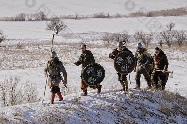 一群拿着盾牌和剑的维京人在冬天的草地上前进。男，领导。