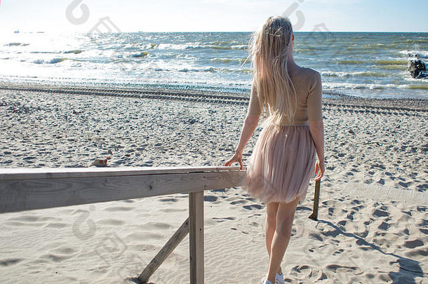 海边年轻快乐的女孩。年轻的金发女郎微笑着。海滩上的年轻女子，自由与自然的统一。后视图