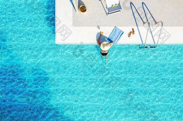 蓝色波浪水池背景与空间的休闲概念。从上方无人机俯视，一名戴着帽子和比基尼的游泳女子