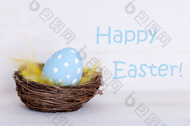 复活节篮子中的一个蓝点复活节彩蛋或白色木质背景上的巢，以英文文本“复活节快乐”作为复活节装饰