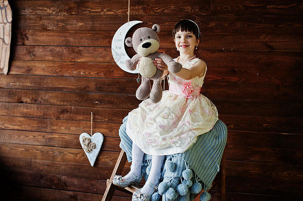 肖像美丽的女孩衣服持有玩具手坐着木梯木墙