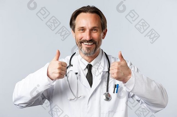2019<strong>冠状病毒</strong>疾病预防、保健人员和疫苗接种的概念。穿着白大褂的英俊满意的医生，高兴地微笑着，竖起大拇指