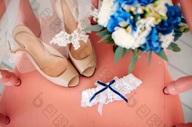 粉红色背景上的一套新娘饰物。带白色和蓝色花朵的婚礼布条、新娘高跟鞋、蕾丝面纱和带b的吊袜带