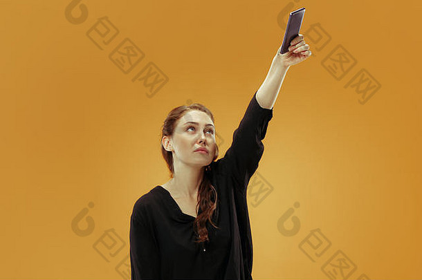 一个自信、快乐、微笑的休闲女孩在金色背景下用<strong>手机</strong>拍摄自拍照片。
