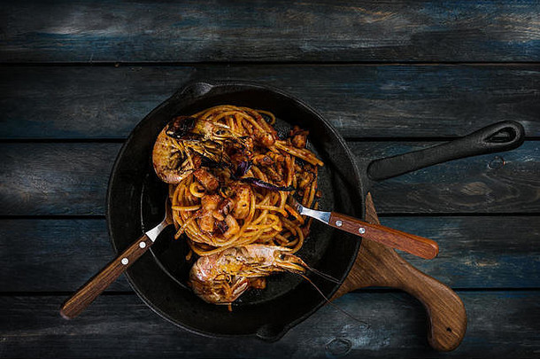 意大利面在热煎锅上用汤匙和叉子在彩色木质背景上煮海鲜意大利面。顶视图。