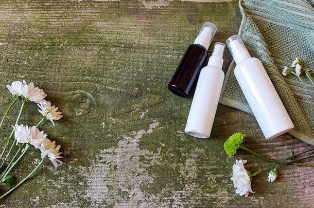化妆品容器，绿色木质背景上的罐子和花朵，俯视图。放在老式桌子上的毛巾和化妆品瓶。