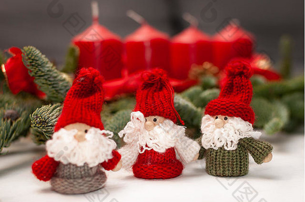 三个小圣诞小矮人站在四根蜡烛和绿杉木树枝前