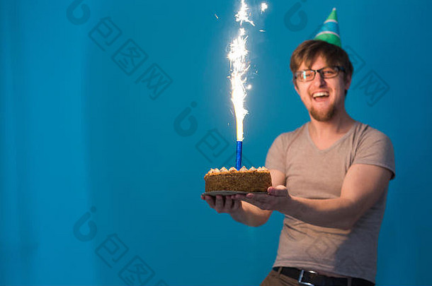 戴着眼镜、戴着纸帽子、手里拿着燃放烟火的蛋糕的疯狂快乐的学生。节日生日概念
