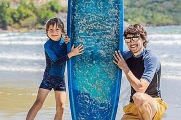 横幅，长格式的父亲或教练教他的儿子如何在假期或假日在海里冲浪。儿童旅游和体育概念