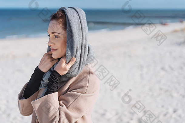 肖像年轻的微笑女人穿外套围巾站海滩
