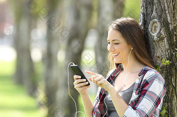 美丽的青少年女孩听选择音乐聪明的电话倾斜树公园