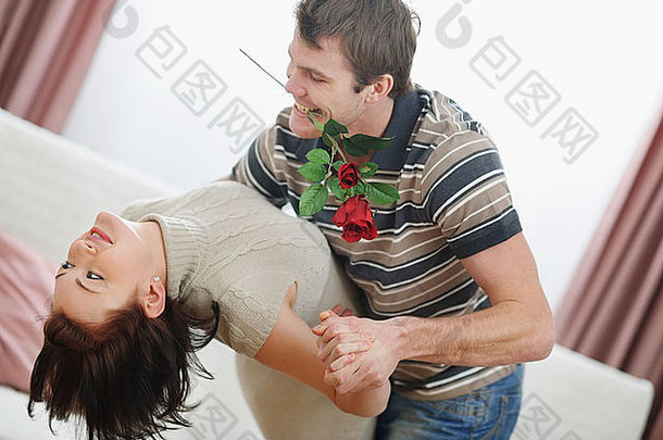 浪漫的年轻夫妇在家里与红玫瑰共舞