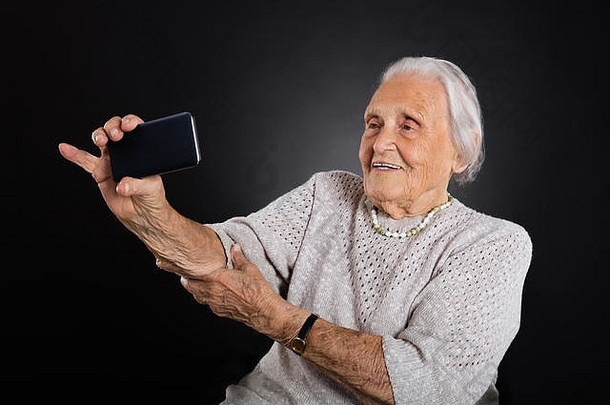 肖像微笑老女人采取自拍智能手机灰色背景