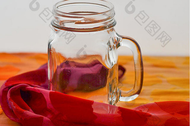 从侧面看，一个透明的空玻璃杯，外面包裹着橙色和红色的丝绸布