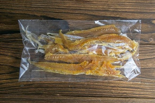 透明包装的干金鱼鱼片开胃品，以比隆木为背景。从小吃鱼到啤酒。闭合
