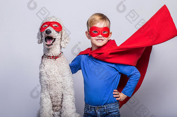 带着狗的英俊的<strong>小超人</strong>。超级英雄万圣节前夕白色背景上的工作室肖像