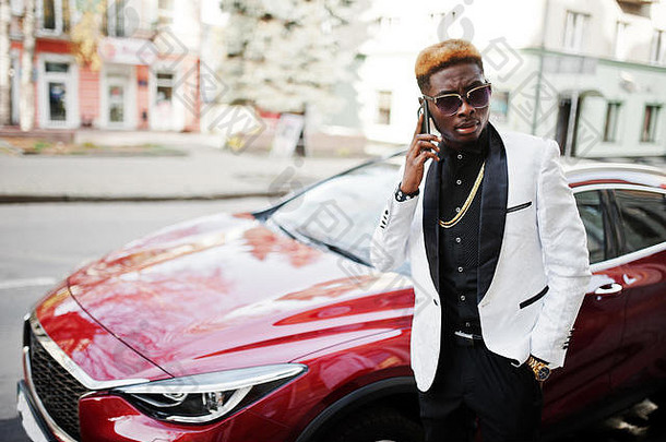 别致的英俊的非洲美国男人。白色西装红色的奢侈品车移动电话手
