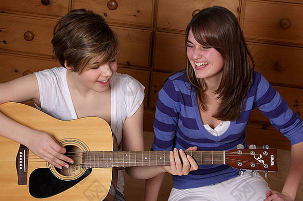 一个十几岁的女孩正在弹吉他，她的朋友在听。