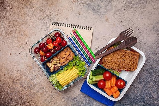 回到学校的概念。有健康新鲜食物的午餐盒。三明治、蔬菜、水果和坚果装在食品容器中，深色背景。