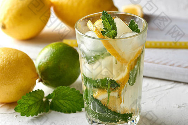 夏日清爽饮料柠檬水，柠檬、薄荷叶、青柠装在玻璃杯中，旁边是制作鸡尾酒的原料