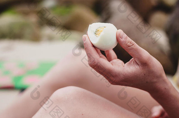 海滩上，一位年轻女子手里拿着一枚鸡蛋