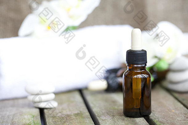 木制表面上的有机兰花纯油滴管瓶。白色的毛巾，人造的兰花头，背景是小溪和鹅卵石。