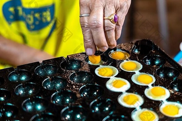 在泰国克拉比镇的克拉比周末夜市上，一位老泰国妇女正在用鸟做煎蛋。