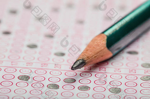 学校学生手拿试卷，手握铅笔在标准化考试的光学表格上书写试卷，并在课堂上做期末考试