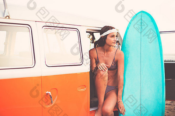 海滩生活方式，美丽的冲浪女孩与经典的老式冲浪车在海滩上日落