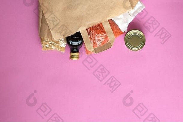 粉红色<strong>背景</strong>的纸袋中的一套各种产品。谷物、罐头食品、意大利面、油。冠状病毒大流行期间的人道主义援助