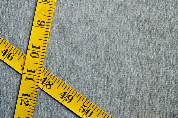 黄色的卷尺，带有厘米或英寸形式的数字指示器，放在灰色针织物上。背景概念